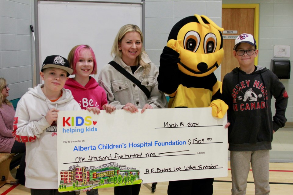 Students at A. E. Bowers Elementary School, Jaime Favell, Thomas Vicei, Noah Kellar, and Toby Conduct, hand off their fundraised cheque to Carmen Dressler, lead for the Kids Helping Kids program at the Alberta Children's Hospital Foundation.