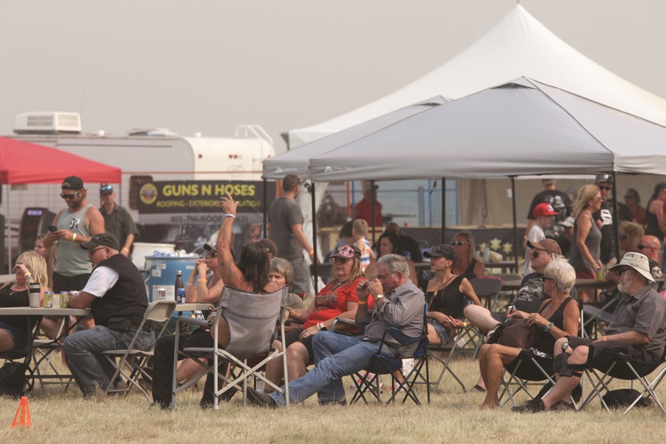 Patrons of the Airdrie Oilmens Association's Bikes & Bulls event enjoy a cool beverage while sitting in the heat and smoke on Aug. 14. Photo by Carmen Cundy/Airdrie City View