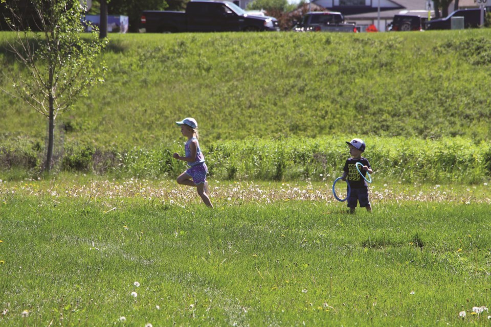 Two children frolic in the grass at Nose Creek Regional Park during the Thumb's Up Foundation's Peace in the Park festival on June 26. 