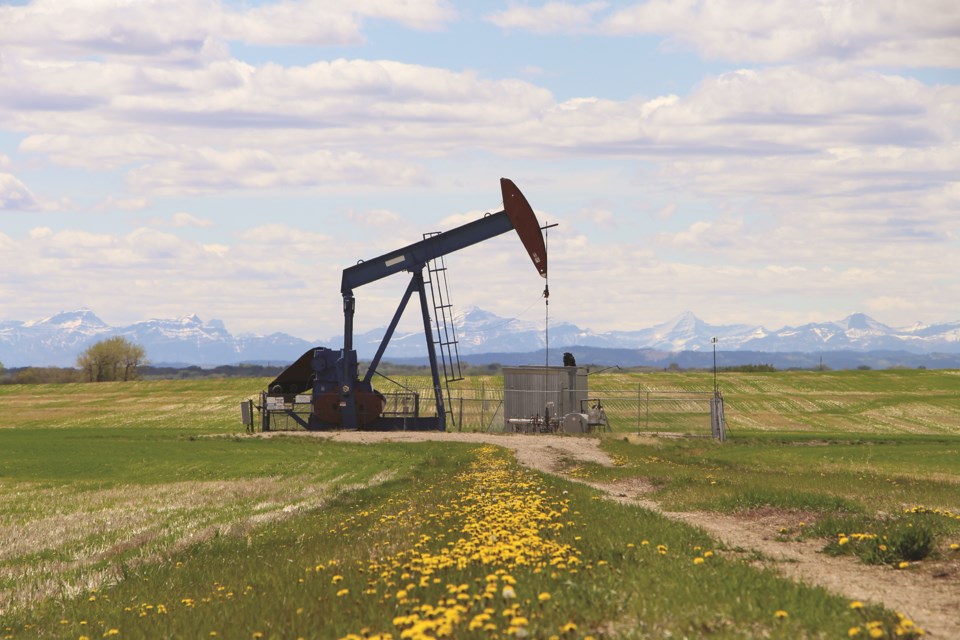The Rocky Mountains are seen behind a pump jack in a farmer's field off of Symons Valley Road.