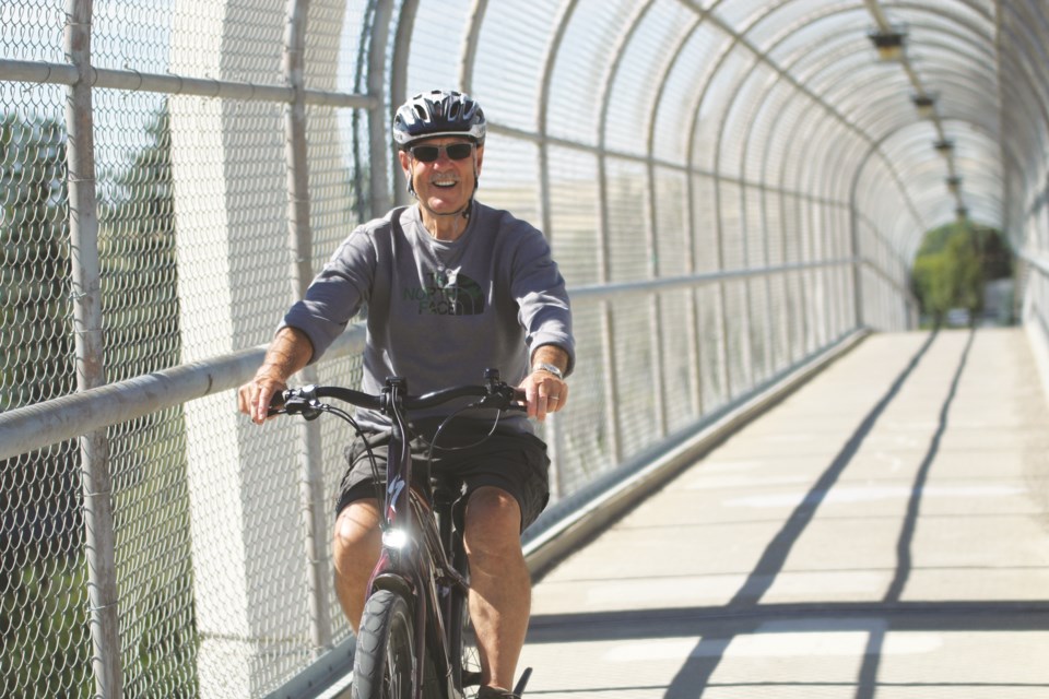 A cyclist smiles as he rides across the Airdrie pedestrian overpass. Photo by Scott Strasser/Airdrie City View 