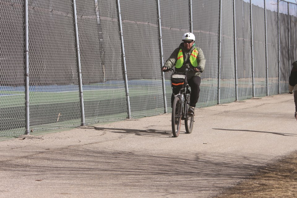 A man wearing a high visibility vest rides his bike on a path along East Lake in Airdrie on a Sunday afternoon.