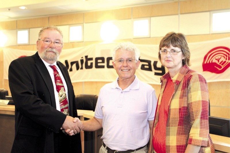 United Way-Chestermere Partnership Chairman Bob Thompson shakes hands with Investment Committee Chair Bill Peddlesden along with Events and Promotions Co-chair Marilyn King