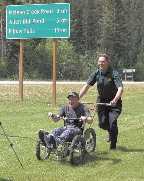 Tourism, Parks, and Recreation Minister Richard Starke pushes volunteer Stephen Henry in the new Park Explorer backcountry wheelchair.