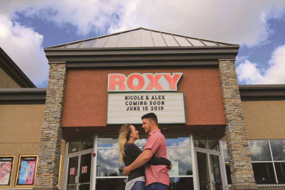 Nicole and Alex Wall, former Roxy Theatre employees, are pictured in front of their 2019 wedding announcement displayed on the Roxy Theatre's marquee sign. 