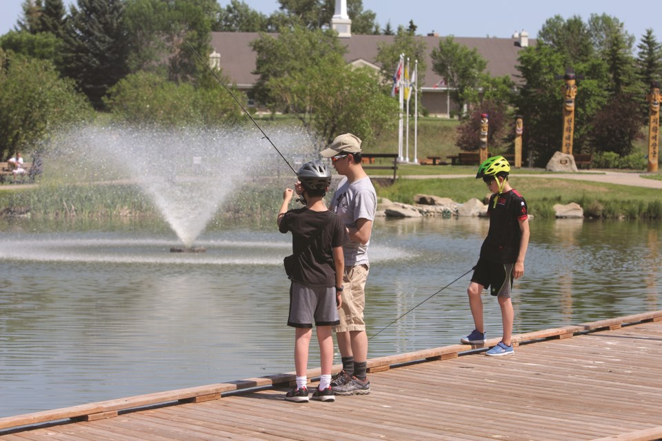 A man teaches two boys how to cast a line in a pond in Nose Creek Park on July 10, 2021. 