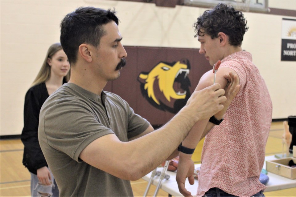 UBC physiotherapy student Jonathan Chow demonstrates a reflex hammer test on the elbow of grade 11 NPSS student Owen Lang at UNBC's healthcare roadshow held at the school May 17, 2022