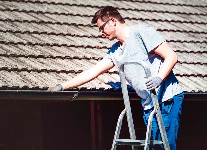 man-high-on-ladder-clearing-leaves-from-gutter-on-house