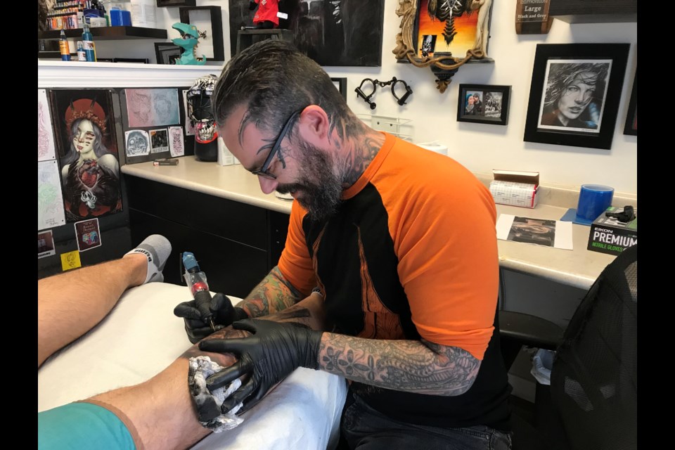 Capital Tattoo artist Lee Robertson works on the calf of Austin Crawford, a 24-year-old steer wrestler from Drayton Valley. Crawford says the tattoo - a U.S. highway scene - is in memory of his late grandmother, Anna Crawford, who passed away earlier this year. Photo; Gary Poignant