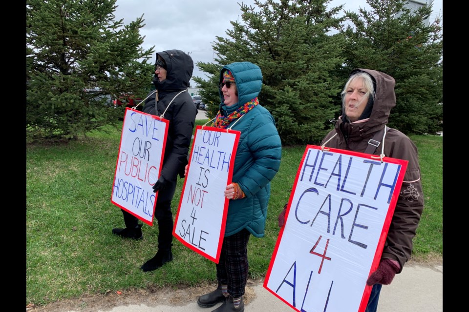 Simcoe County Health Coalition board member and retired nurse Victoria Scott, Engage Barrie member and retired social services worker Anita Johnson-Ford, and Jenny Pilbeam-Harting, first vice-president of PCAC Barrie area council carry signs showing their support of keeping Ontario's health-care system public during an event on Tuesday. 