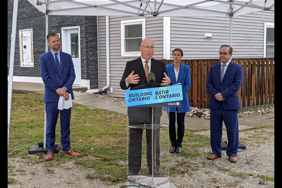 Ontario Minister of Municipal Affairs and Housing Steve Clark speaks, while Greg Bishop of the County of Simcoe, left, and Barrie-area MPPs Doug Downey and Abdrea Khanjin look on Tuesday morning.