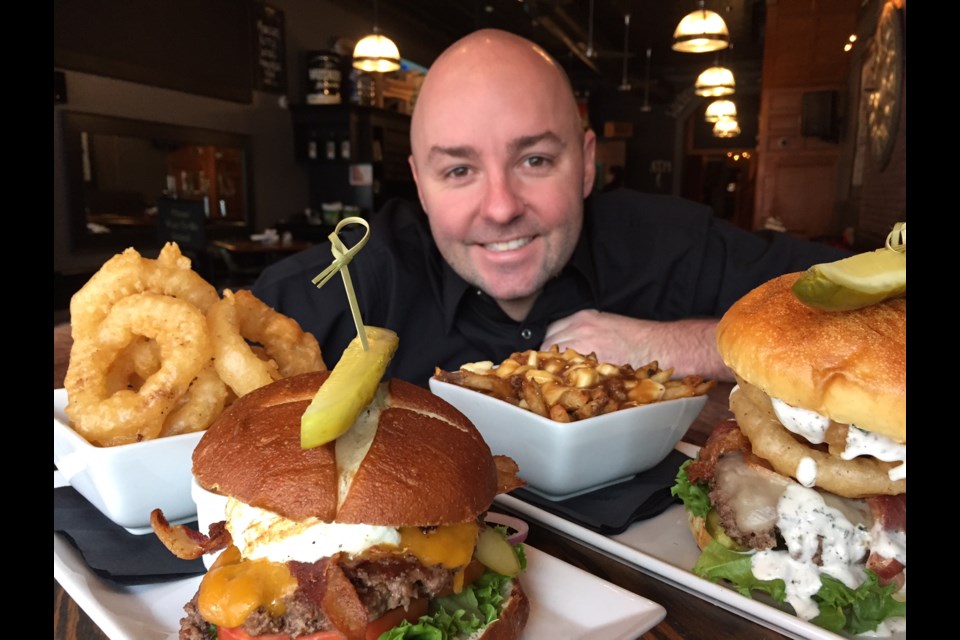 Kenzington Burger Bar owner Brandon Clark poses with the Rodeo and Kenzie burgers decked out with sides of poutine and onion rings.  Sue Sgambati/BarrieToday