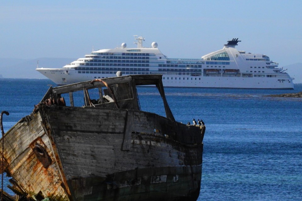 A Second World War mine sweeper, a wooden wreck, is shown in the foreground against the Seabourn Quest in the background, Falkland Islands.