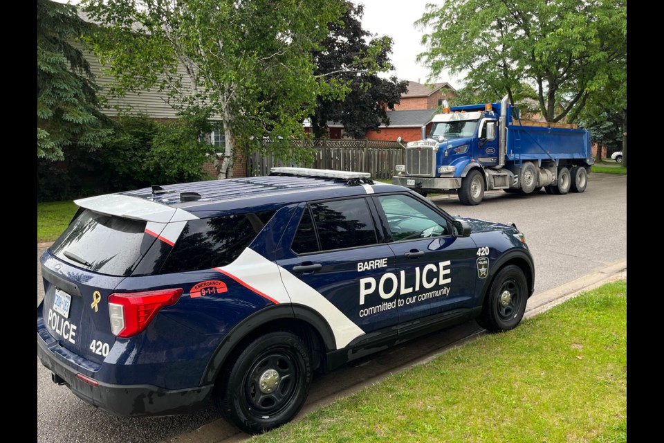 A Barrie police officer keeps an eye on a dump truck on Archer Street in the city's south end, Wednesday morning. 