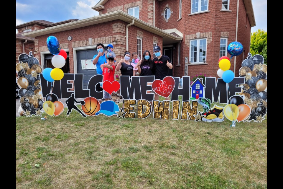 Edwin Ng's children and grandchildren give the thumbs up by the welcome home sign on the family home's front lawn.