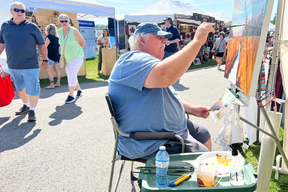Artist Kevin Joyce, of Lindsay, works on a landscape painting as visitors go by at Kempenfest in Barrie