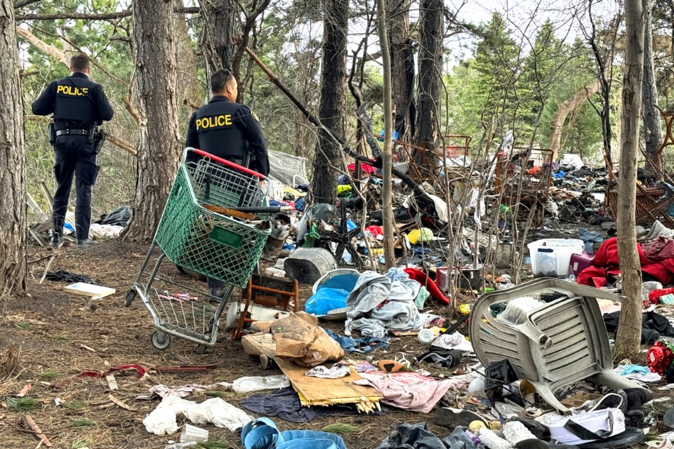 OPP officers walk through the garbage and debris in a treed area of the Highway 400 and Bayfield Street interchange where a homeless encampment was situated. It was also the site of a recent fire. Cleanup of the site began today.