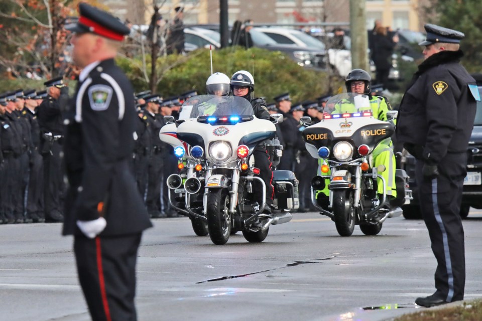 Police officers line the street outside Sadlon Arena in south-end Barrie, Thursday, as a motorcycle escort leads the hearses on Bayview Drive during the final stretch of the funeral procession for the two South Simcoe slain officers, Morgan Russell and Devon Northrup.