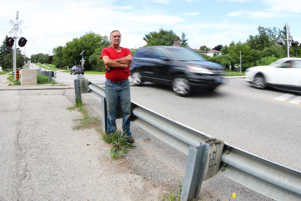 Concerned resident Roger Natale watches vehicles climb the steep grade leading up to railroad tracks on Little Avenue in south-end Barrie where a Tesla launched iinto the air Tuesday night before crashing in the parking lot of Assikinack Public School. A 46-year-old man has been charged. Kevin Lamb for BarrieToday