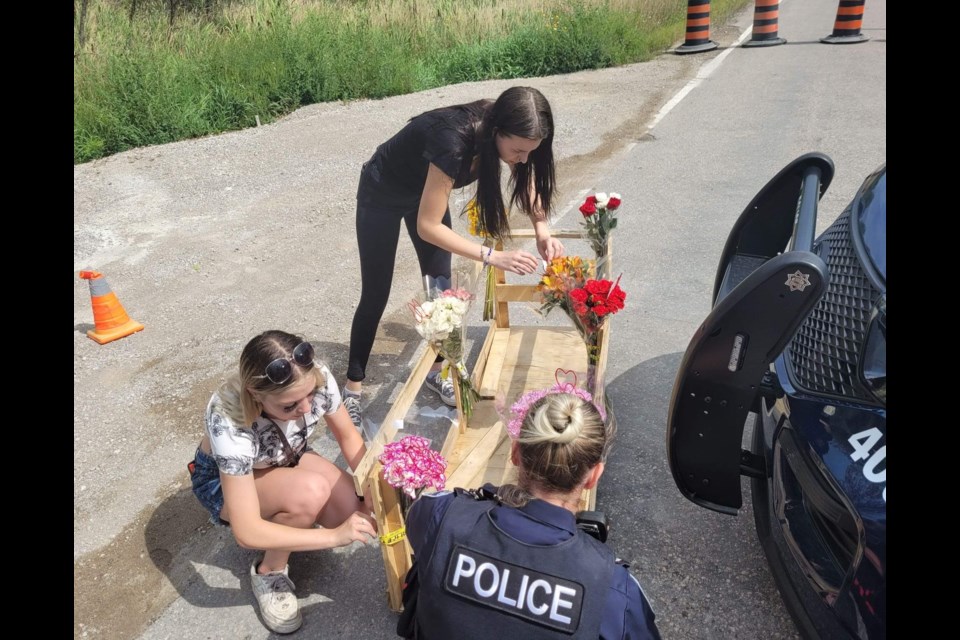 A Barrie police officer helps two young women place flowers at a makeshift memorial, Monday, on McKay Road near the scene where six young people died in a weekend crash. 
