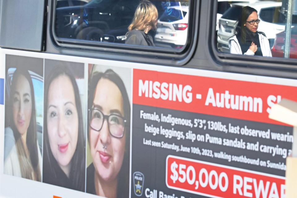 Lili-Anne Moore, the sister of Autumn Shaganash, right, reflected on a bus window, watches a news conference at Barrie police headquarters on Tuesday, April 9. City police are using bus signs and billboards to help find Shaganash, who has been missing since June 2023.