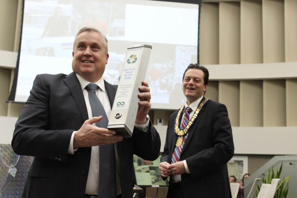Former city councillor Doug Shipley, left, was honoured during a meeting on Monday, Feb. 10, 2020. He's holding a cigarette butt disposal container, an initiative he spearheaded in the city. At right is Mayor Jeff Lehman. Raymond Bowe/BarrieToday