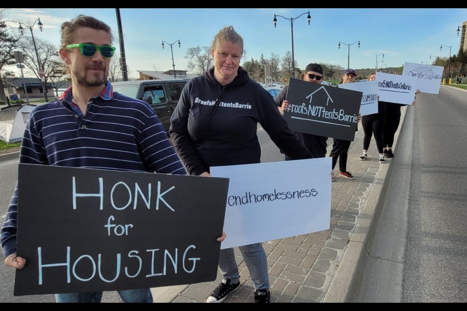 Alec Wilding, front, and many others stand beside a busy Lakeshore Drive to bring awareness to the region's housing crisis, Wednesday morning.  