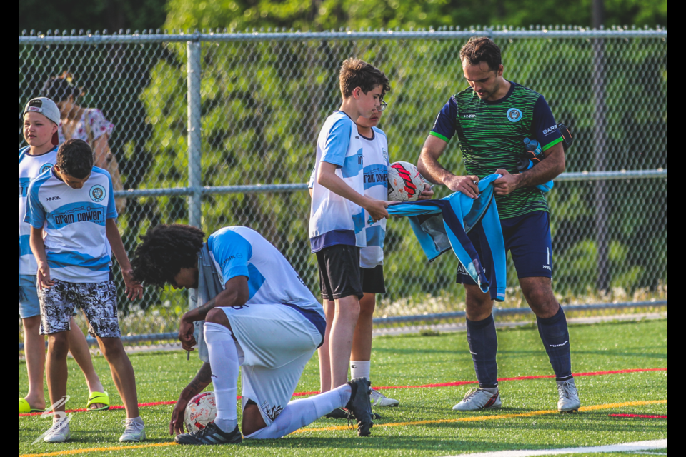 Simcoe County Rovers FC players Jah'Moises Corona (kneeling) and goalkeeper Ricky Gomes sign autographs and talk to kids after the Rovers' last home game. 
