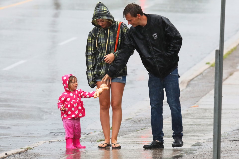 A young lady hands over her doll during a rain shower on Dunlop Street in Barrie on Sunday, July 22, 2018. Kevin Lamb for BarrieToday.