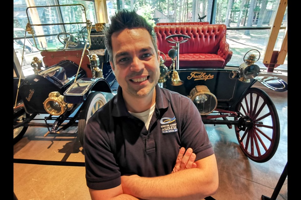 Forrest Patenaude, education supervisor at the Simcoe County Museum, stands in front of classic, classic cars on display at the museum.