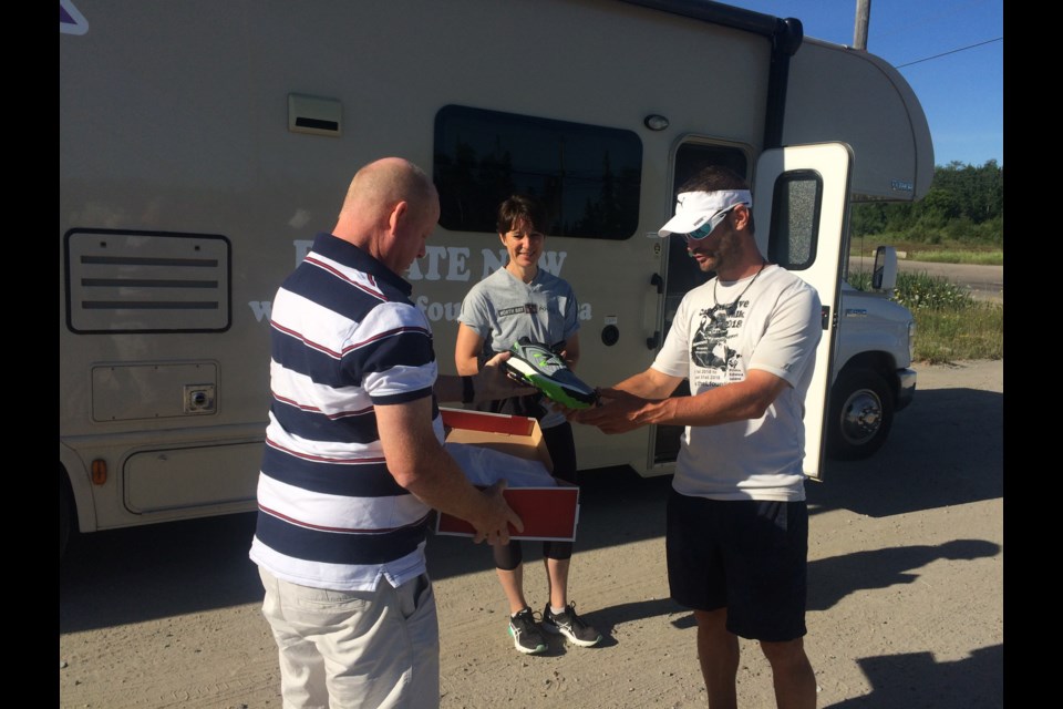 Andrew Greig of Foot and Sole donates a new pair of shoes to Jimmy Lefebvre to help complete his walk to PEI, as Aline Major a civilian with the North Bay Police Service looks on.