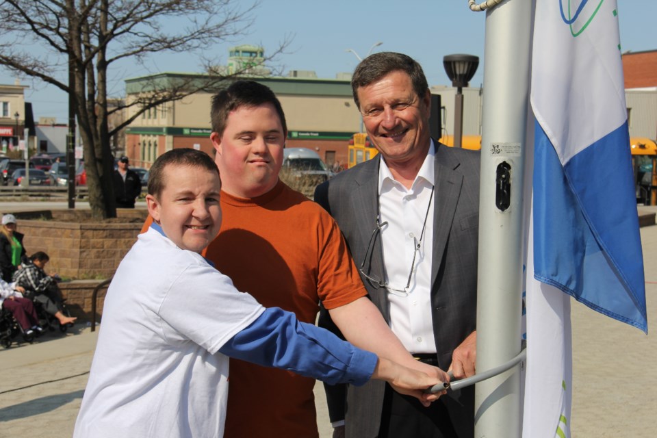 Mathew Tresnak and Mathew Abraham help Councillor Mark King raise the flag at City Hall to kick off Community Living month. Photo by Jeff Turl.