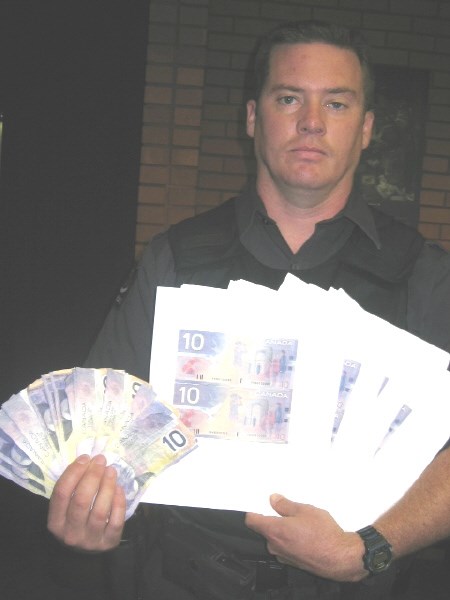 Cst. Bill Gainforth holds phoney ten-dollar bills and uncut photocopies. Photo by Phil Novak.