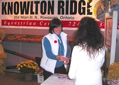 Bobbie Cardwell hands out literature at the Knowlton Ridge Equestrian Centre booth at the Royal Agricultural Winter Fair.  FedNor created a beautiful Northern Ontario village booth at the Fair, and several regional companies were represented, including this Powassan-based equestrian centre.