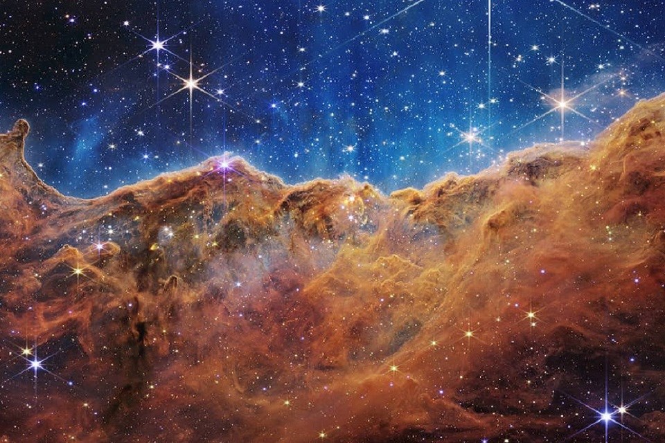 One of the first images captured by the James Webb Space Telescope, this landscape of “mountains” and “valleys” speckled with glittering stars is actually the edge of a nearby young star-forming region called NGC 3324 in the Carina Nebula. 