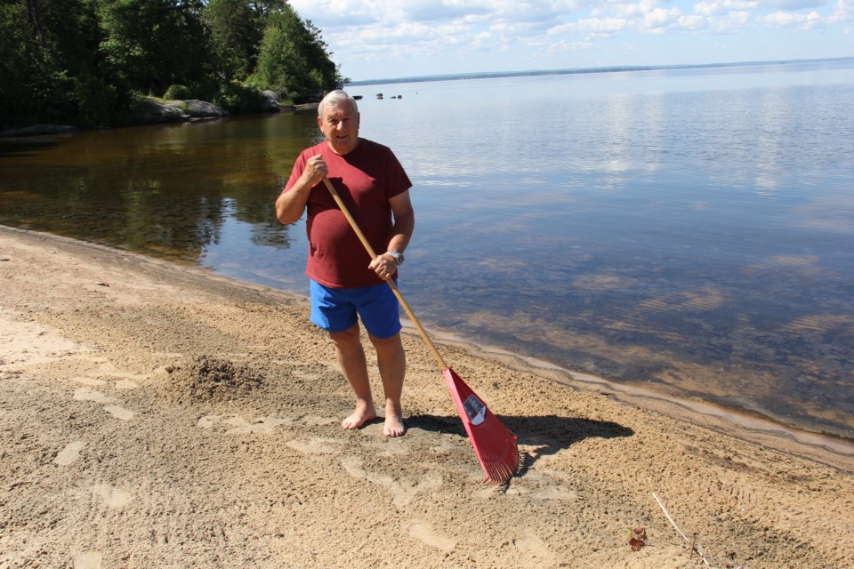 USED 170706 1 Brian Baldwin rakes up piles of dead shad flies on his beach. Lake Nipissing. Photo by Brenda Turl for BayToday.