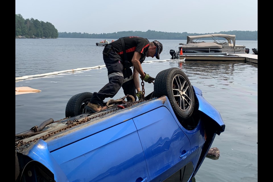 Larry Bartlett, owner of Bartlett's Towing puts hooks underneath the carriage of a car that smashed through a guard rail and into Trout Lake.  Photo by Chris Dawson/BayToday. 