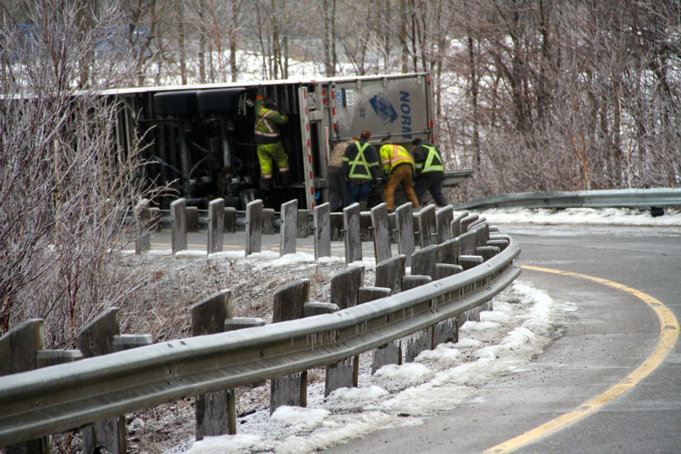 Workers looking at the tipped over transport trailer that lost control on the slippery off ramp.  Photo by Chris Dawson.  
