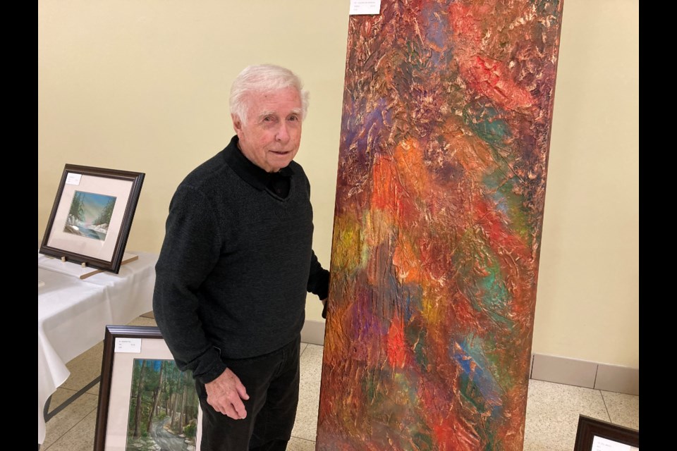 Artist Jack Lockhart stands beside one of his textured art pieces