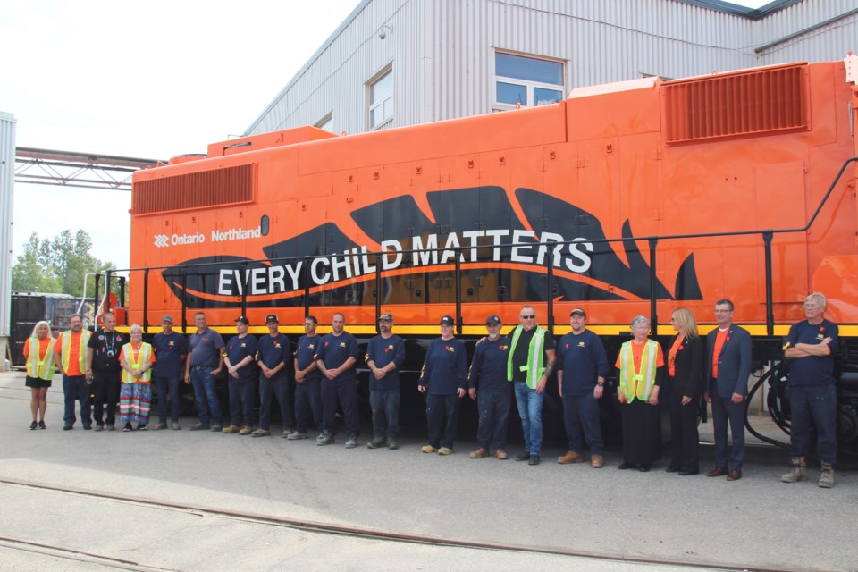 Nipissing First Nation members, Ontario Northland painters, executives, and others pose before the freshly minted Every Child Matters locomotive / Photo by David Briggs