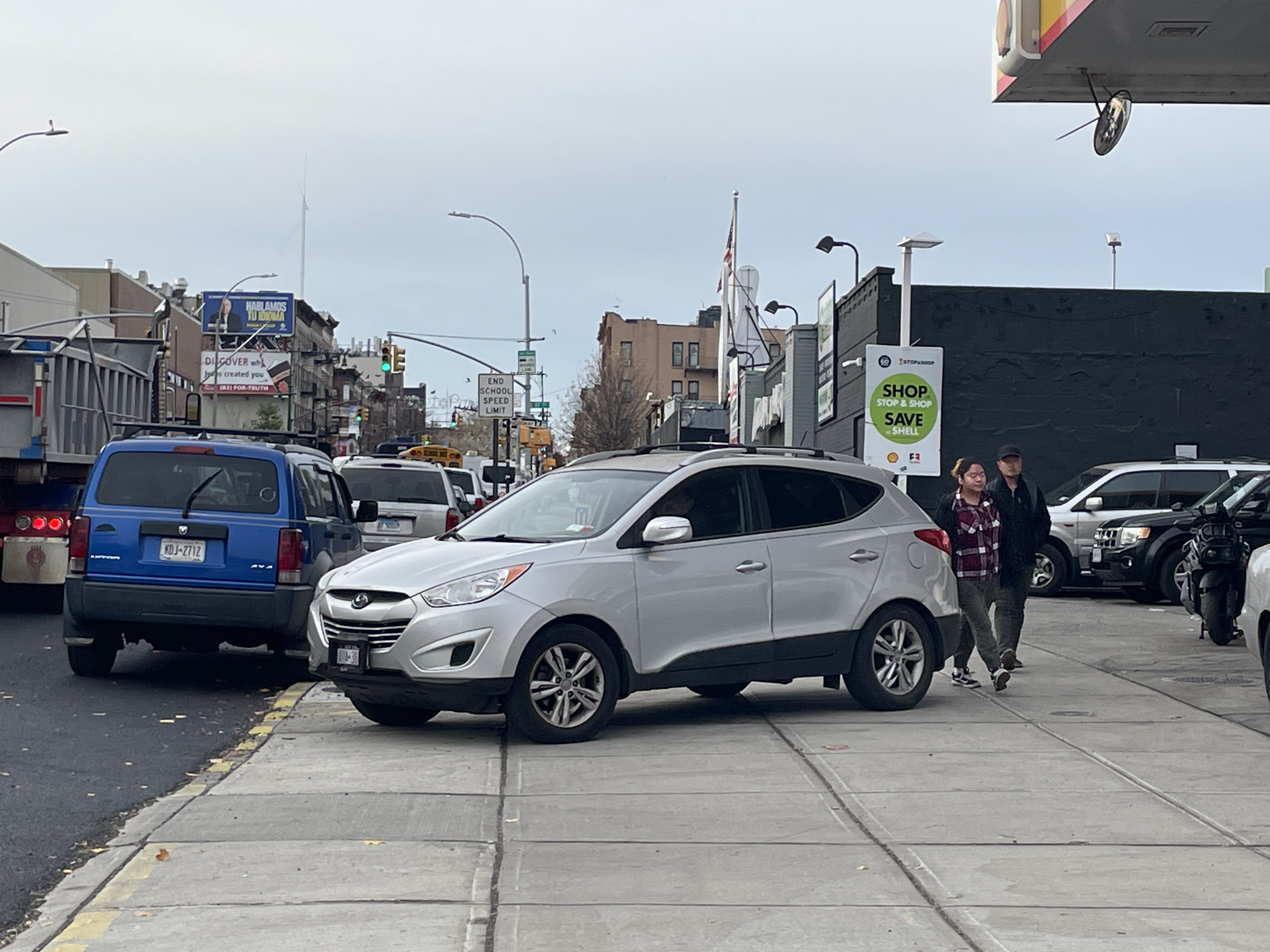 Students on their way to school walk around cars coming out of a gas station