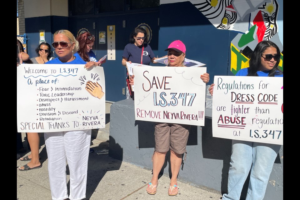 Three participants in I.S. 347's press conference hold up signs calling out Principal Neyva Rivera's treatment of the school community.