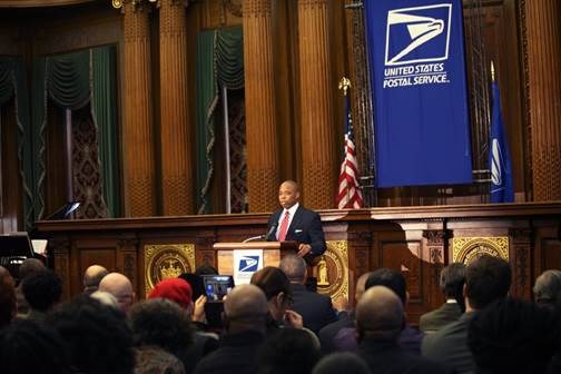 Brooklyn Borough President Eric Adams (left-center) commemorates the unveiling of the new United States Postal Service's Forever stamp in honor of Shirley Chisholm at a ceremony inside Brooklyn Borough Hall
