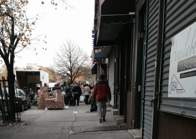 Volunteers load boxes of food and people line up down the block to receive donated food items at the Bed-Stuy Campaign Against Hunger