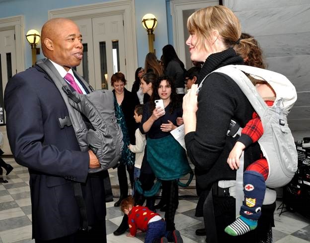 Brooklyn Borough President Eric L. Adams, wearing one of the baby carriers donated by Delta Children talking with BirthFocus Executive Director Elizabeth Mangum-Sarach, who was sporting a baby carrier of her own to hold her young son.                                            Photo Credit: Erica Sherman/Brooklyn BP's Office