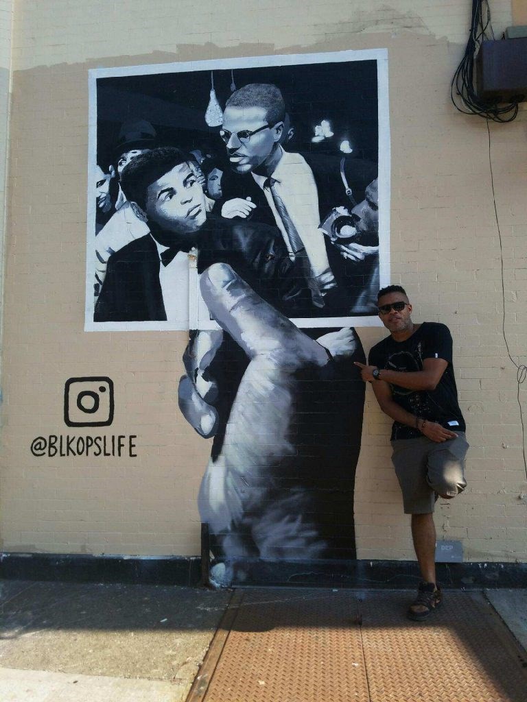 Artist Brian Deka Paupaw stands in front of his brand-new mural, "Hand of Peace," located on the corner of Putnam Avenue and Malcolm X Blvd. in Bed-Stuy