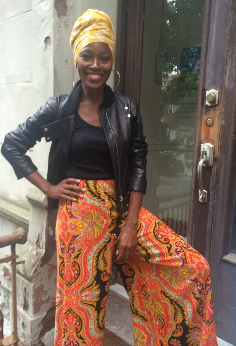 Sheryl Roberts poses in a Indigo Style Vintage ensemble in front of her Greene Ave house. Black leather jacket over a black shirt on top of loose orange patterned trouser skirt