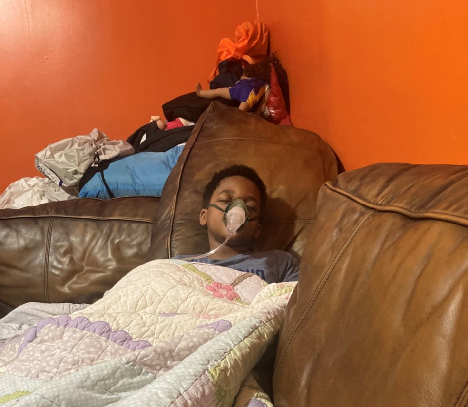 Ikorine Fairclough's young son lies on a couch wearing a visible oxygen mask.