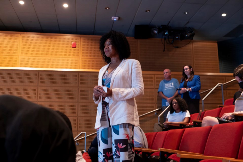 A woman wearing a blue dress and white cardigan stands up to hear Sen. Gillibrand's response to her question.