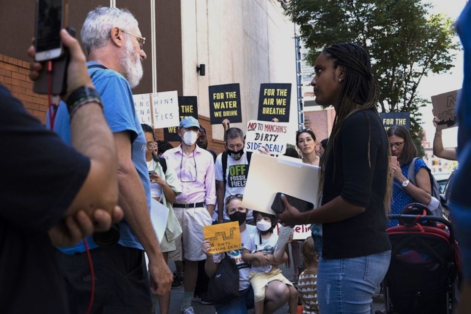 In the foreground, an activist speaks with a representative from Hakeem Jeffries' office. Through the space between them are other activists holding signs and watching intently.